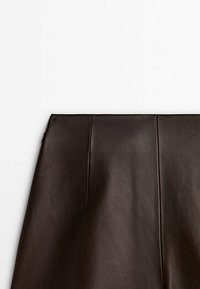 Jupe en simili-cuir marron foncé avec des coutures verticales, affichée à plat sur un fond blanc.