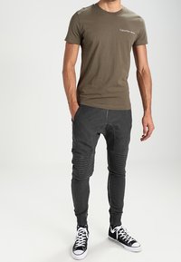 Olivgrönt t-shirt med "Calvin Klein Jeans"-logotyp, i kombination med texturerade svarta joggers med ribbade detaljer och vita sneakers.