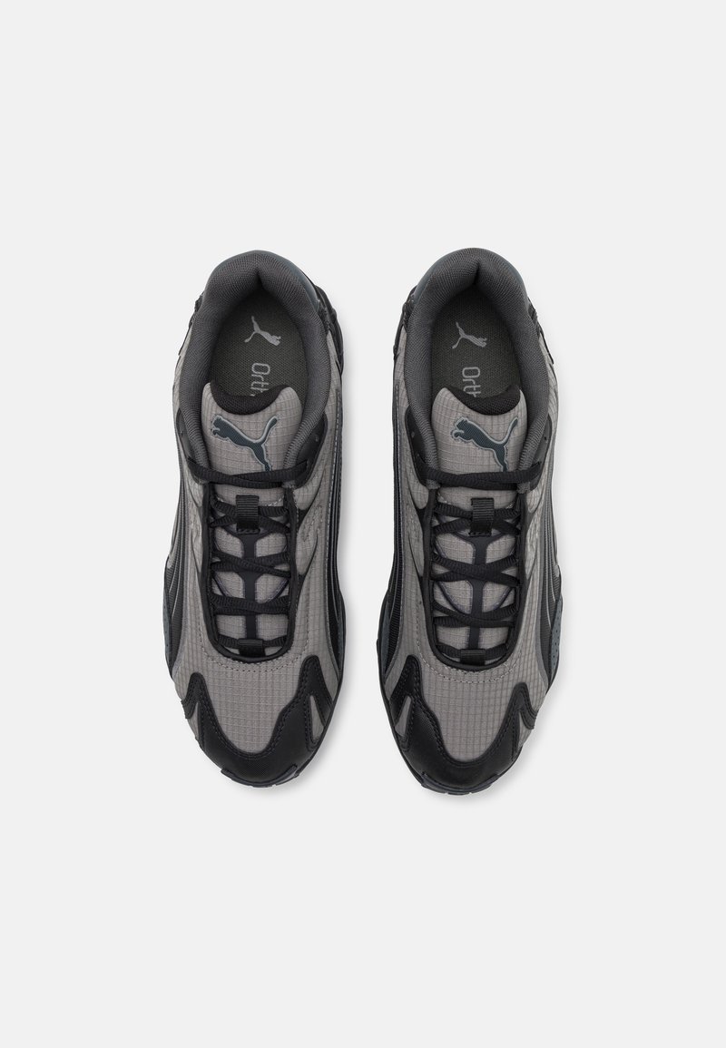 Graue Sportschuhe mit strukturierter Oberfläche, schwarzen Akzenten und einer gepolsterten Sohle. Mit Schnürsenkeln und Logodetail auf der Zunge.