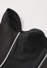 Vêtement noir avec une finition en tissu lisse et un patch texturé et respirant. Présente un col rond, des accents rayés et un design d'épaule arrondie.