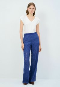 Pantalones de pata ancha de color azul con un diseño texturizado y cintura alta, combinados con una camiseta básica blanca con escote en V.