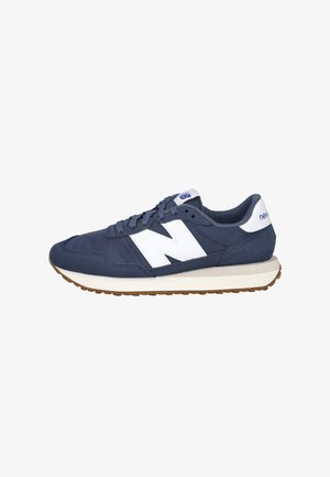Zapatilla New Balance azul marino con logo blanco "N", pestaña blanca en el talón, suela de goma y diseño con cordones sobre un fondo blanco.