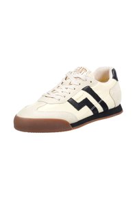 Bílé semišové tenisky s černými geometrickými pruhy a hnědou gumovou podrážkou. Obsahují béžové tkaničky a logo na jazyku.