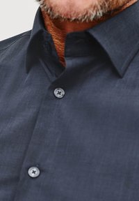 Granatowa koszula z guzikami, wykonana z textured tkaniny. Posiada klasyczny kołnierzyk, dwa guziki oraz kontrastowy detal przy wewnętrznej części kołnierza.