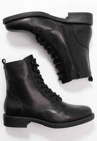 Botas de tobillo de cuero negro con una textura suave, que cuentan con un cierre de cordones en la parte delantera y una cremallera lateral para un acceso fácil, y un tacón bajo y resistente.