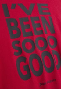 Piros póló nagy fekete szöveggel: „IGEN JÓ VOLTAM.” Kicsi „Juicy Couture” logó a szegély közelében. Simább tapintású anyag.