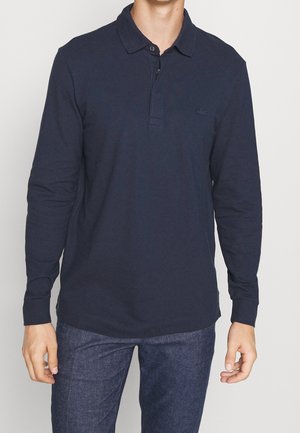 Polo à manches longues bleu marine avec col plat, patte de boutonnage à un seul bouton et logo discret sur la poitrine. Confectionné dans un tissu lisse, semblable au coton.