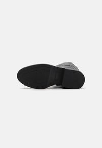Suela negra texturizada de una bota con un borde suave y una ligera curva, que presenta detalles de costura y un área de etiqueta minimalista.