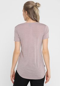 Ljusrosa t-shirt med kort ärm och rundad fåll, gjord av mjukt, texturerat tyg. Diskret melerat mönster, enkel baksida, minimalistisk design.