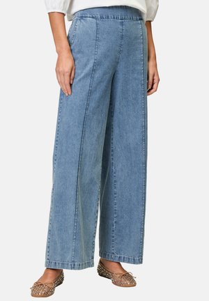 Jean large en denim bleu clair avec une texture lisse, présentant des coutures avant et une coupe décontractée, associés à des chaussures plates à motifs.