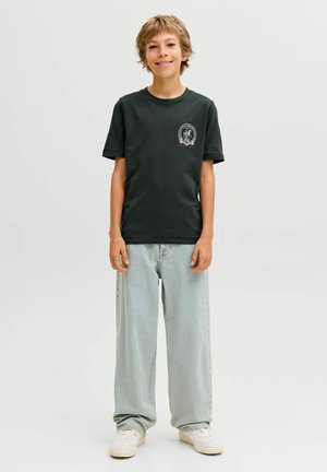 T-shirt en coton vert foncé à manches courtes, avec un col rond et un petit graphique sur la poitrine gauche. Associé à un jean bleu clair.