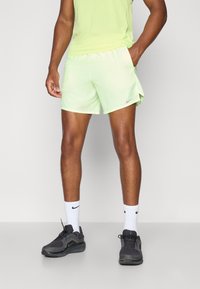 Pantaloni corti da corsa verde chiaro con cintura elastica e tasche laterali. Indossati con scarpe da ginnastica nere e calzini bianchi, con un logo.