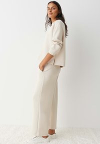 Licht beige loungewear-set met een sweatshirt in een relaxte pasvorm, voorzien van geribbelde manchetten, en wijde broek met zijzakken. Glad van textuur.