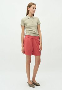 Khaki polo tričko s krátkymi rukávmi a tromi gombíkmi, spárované s koralovými šortkami so elastickým pásom. Model nosí špicaté balerínky.