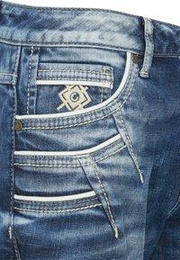 Blaue Denim-Jeans mit einer ausgewaschenen Optik und kontrastierenden weißen Nähten, die mehrere Gesäßtaschen und ein besticktes Logodetail aufweisen.
