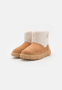 Brune semskede ankelstøvler med en hvit faux shearling krage, teksturert overflate og en tykk beige gummisåle. Har en logo på siden.
