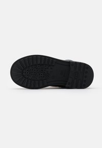 Semelle de chaussure en caoutchouc noir avec un motif de grip texturé, comprenant des indentations circulaires et linéaires pour une traction améliorée. Design durable et flexible.