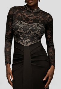 Zwarte jurk met een kanten lijfje en lange mouwen, met bloemmotieven en een nauwsluitende rok die elegant valt.