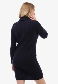 Tumes nööriga kampsun-kleit kõrge kraega ja pikkade varrukatega, ribakujundusega mansetid ja alläär, sile tekstuur. Näidatud tagantvaade.