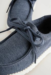 Marineblaue Leinenschuhe mit strukturiertem Obermaterial, runder Zehenpartie und weißer Gummisohle. Mit passenden Schnürsenkeln, die zu einer Schleife gebunden sind.