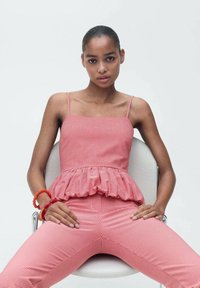 Red gingham peplum top with thin straps and matching fitted pants, featuring a textured fabric and ruffled hem. Accessories include a red bracelet.