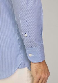 Camicia a righe blu e bianche con maniche lunghe, polsini con bottoni e vestibilità sartoriale. Il tessuto appare liscio con dettagli di trama fine.