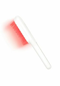 Brosse électronique manuelle blanche pour le cuir chevelu émettant une lumière rouge à partir de ses poils en silicone, inclinée sur un fond blanc.