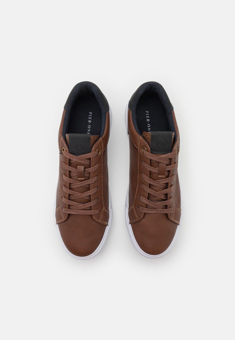 Baskets en cuir marron avec des perforations, semelle en caoutchouc blanche, bout rond et lacets plats. Accents noirs au niveau du talon et de la languette.