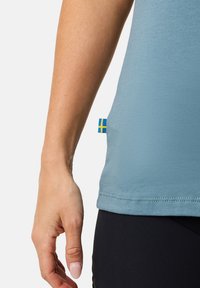 Light blue short-sleeve shirt with a smooth texture, featuring a small yellow and blue Swedish flag tag at the bottom left.