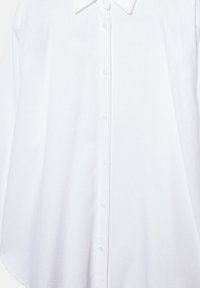 Chemise blanche à manches longues avec col et boutons, dotée d'un tissu lisse et de sept boutons visibles sur le devant.