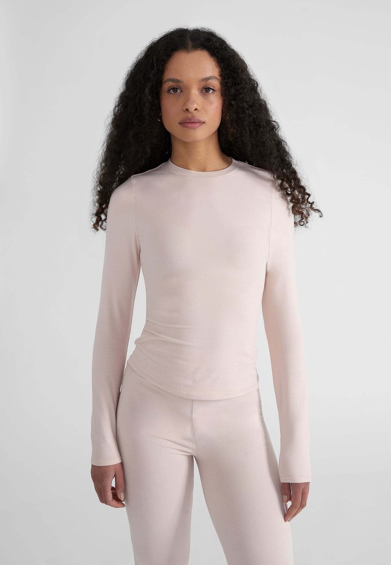Maglia a maniche lunghe, colletto rotondo, di colore rosa chiaro, realizzata in tessuto morbido. Il design presenta uno stile aderente con spalle senza cuciture e maniche lunghe.