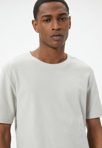 Camiseta de manga corta en gris claro con cuello redondo y un acabado texturizado. Diseño sencillo, sin patrones ni acentos visibles.