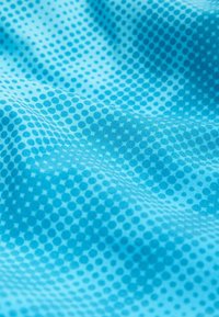 Textil, amely különböző méretű kék pöttyöket ábrázol világosabb kék háttéren, sima és enyhén texturált felülettel.