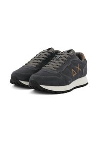 Sneakers in suede grigio scuro con lacci grigi, suola intermedia bianca e suola esterna in gomma nera. Presentano il logo del marchio e un design geometrico in marrone.
