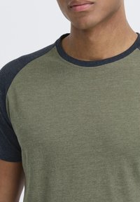 Green short-sleeve t-shirt with dark blue raglan sleeves. Made of soft fabric, features a crew neckline and a smooth texture.