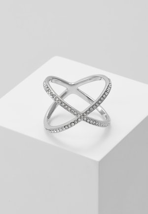 Zilveren ring met een open kruispatroon, versierd met kleine heldere kristallen langs de elkaar kruisende banden, tentoongesteld op een wit voetstuk.