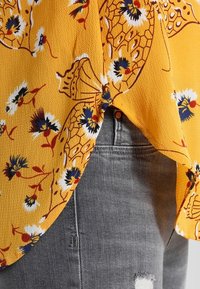 Un tessuto a fiori gialli infilato in jeans di denim grigio chiaro con un strappo danneggiato vicino al ginocchio.