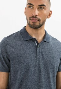 Granatowa koszulka polo z teksturowanej tkaniny, z krótkimi rękawami i zapięciem na dwa guziki. Posiada subtelne logo na klatce piersiowej.