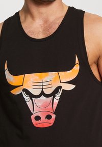 Homme portant un débardeur noir avec un visage de taureau stylisé en dégradé orange, rouge et blanc sur la poitrine.