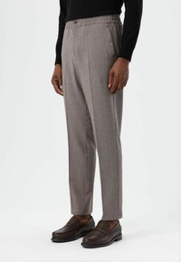 Grijze geruite broek met elastische tailleband en knoopsluiting. Heeft een rechte pasvorm en een subtiele textuur. Gecombineerd met bruine loafers.