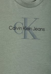 Grünes Baumwoll-T-Shirt mit dem Schriftzug "Calvin Klein Jeans" und einem großen "CK"-Logo. Rundhalsausschnitt mit weicher Textur.