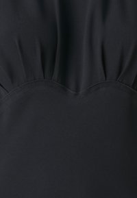 Crna tkanina glatke teksture sa nabranim detaljima na vrhu i šaljastim izrezom. Dizajn je minimalistički i elegantan.