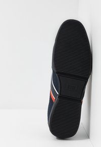 Sneaker in tessuto blu navy con suola in gomma nera, caratterizzata da strisce bianche e rosse. La suola presenta un motivo di presa testurizzato e un marchio.