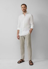 Weißes Leinenhemd mit langen Ärmeln, beigefarbene maßgeschneiderte Hose und braune Sandalen mit Riemen. Einfaches, sauberes Design mit subtiler Textur.