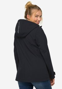 Veste imperméable navy avec capuche ajustable, fermeture éclair à l'avant et poches latérales. Comprend un logo brodé au dos et un tissu texturé.