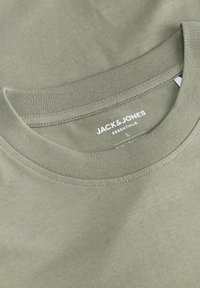 Oliwkowa bawełniana koszulka z okrągłym dekoltem. Posiada metkę "JACK & JONES ESSENTIALS" oraz metkę rozmiaru na wewnętrznej stronie kołnierza.