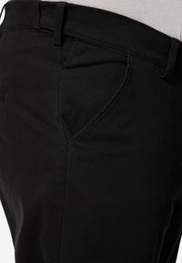 Černé bavlněné kalhoty s běžným pasem, bočními kapsami, hladkou texturou a viditelnými švy podél švů.