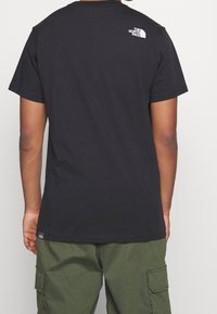 Camiseta de algodón negra con cuello redondo, con un pequeño logo blanco en la parte superior de la espalda y una etiqueta en el dobladillo inferior.