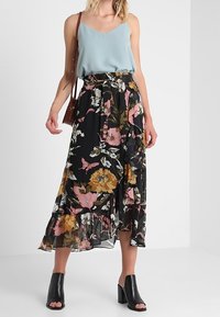 Jupe midi fleurie noire, ornée d'un mélange de fleurs roses, orange et blanches. Tissu léger et fluide avec un ourlet à volants. Associée à un haut bleu clair.
