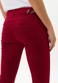 Vaqueros de mezclilla rojos con una textura suave, un diseño ajustado y bolsillos traseros. La cinturilla presenta un detalle de patrón para un toque adicional.